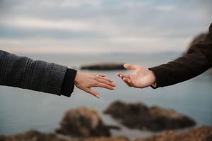 Two hands reaching towards each other against a moody cloudy sky background in a dramatic gesture of connection.