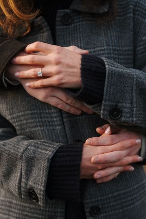 Close-up shots of hands wearing an engagement ring against a dark gray wool sweater background.