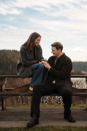 A couple shares an intimate moment on a wooden bench overlooking a scenic winter landscape.