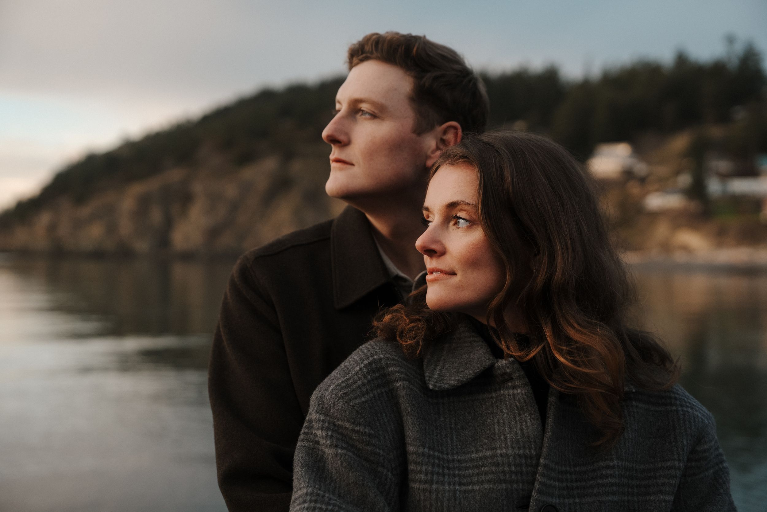 A couple shares an intimate moment by a serene lake at sunset, surrounded by rocky cliffs and natural scenery.