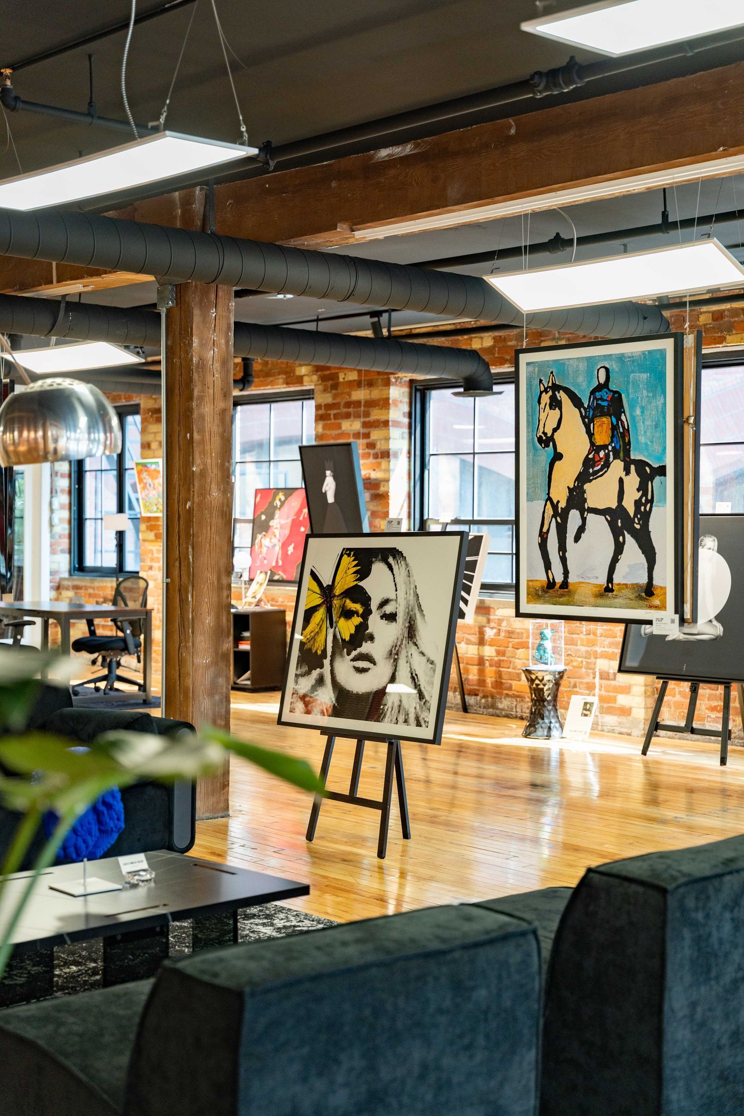 Modern office space with exposed brick walls features black silhouette artwork and hardwood floors in an open layout design.
