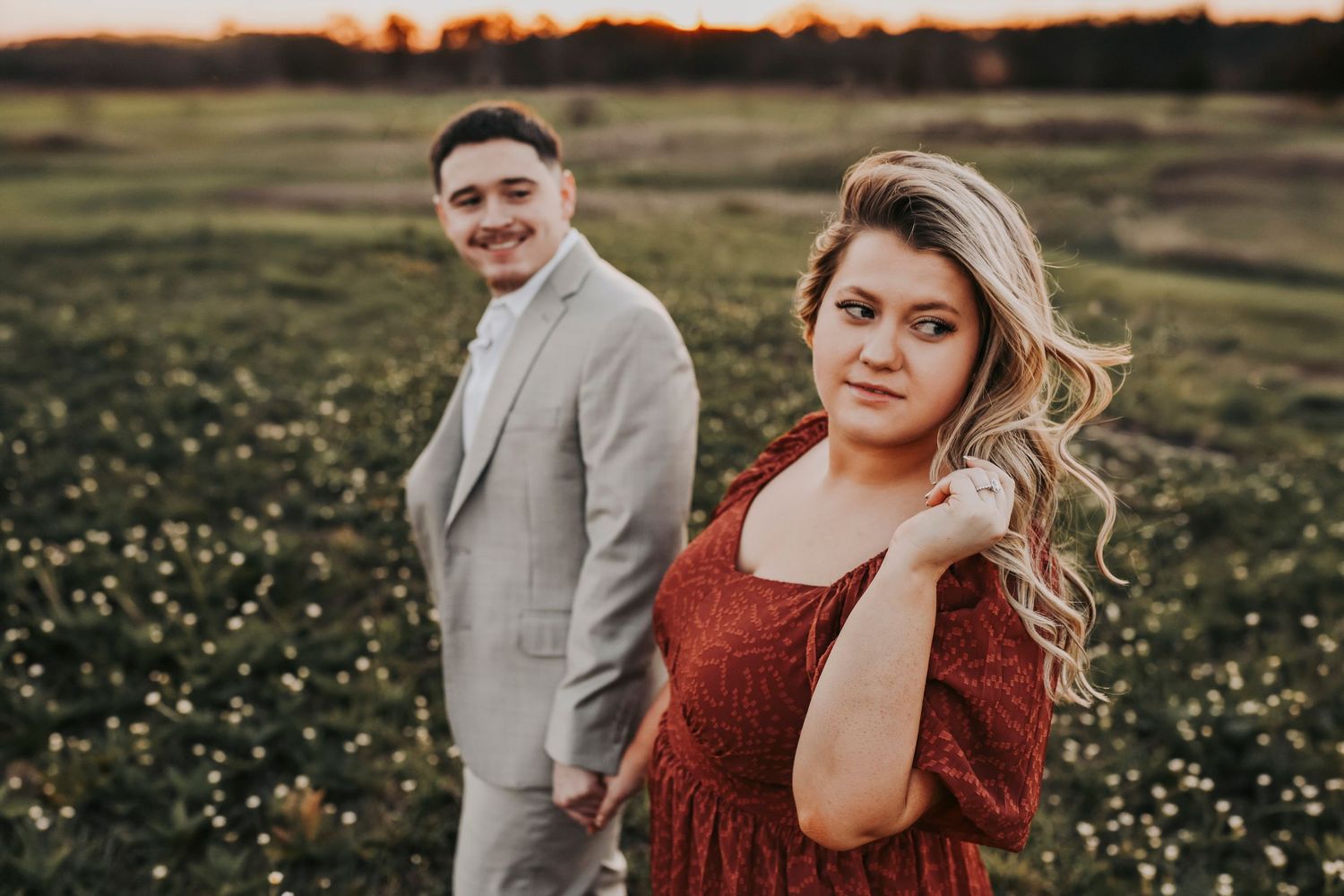 Hunter and Gavin walking through a green field during their engagement session at Murrell Park in Flower Mound, Texas.