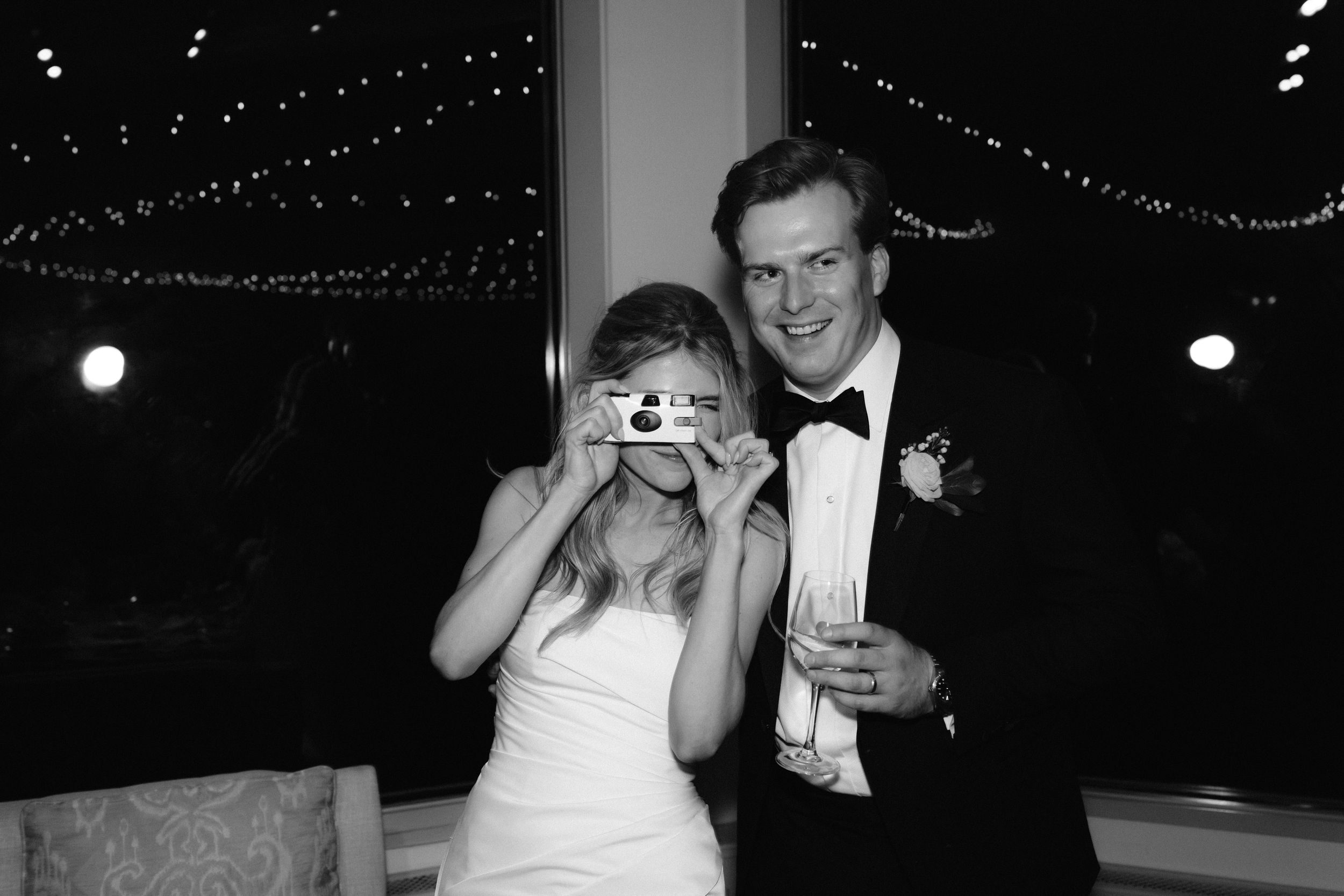 Couple dances together at a wedding reception under twinkling lights and decorative string lighting.