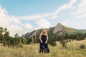 aurora high school senior photo of a girl in front of a panoramic view of rolling hills and mountains under blue skies on a sunny day.