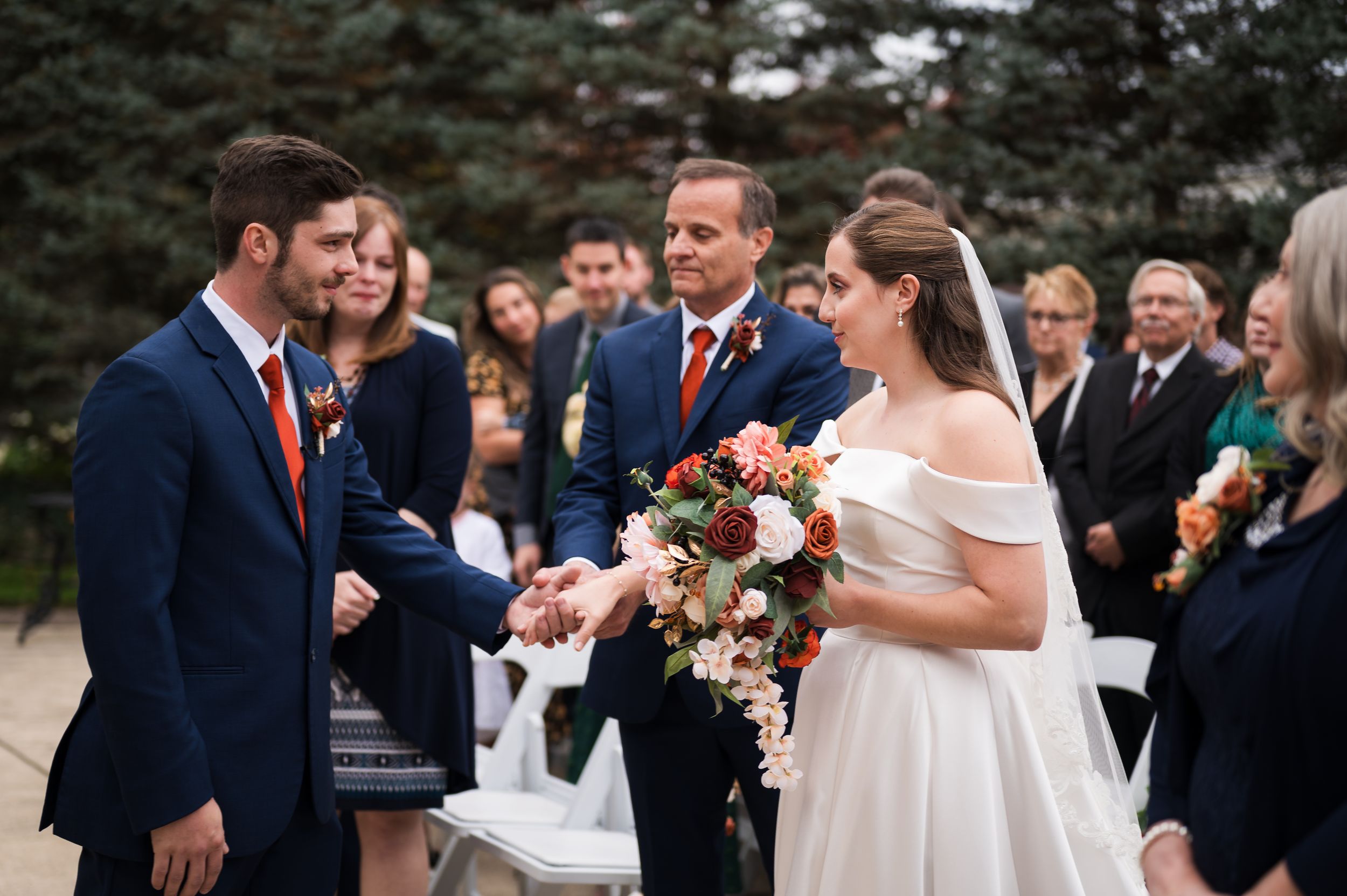 A couple in wedding attire shares a romantic moment outdoors surrounded by autumn foliage.