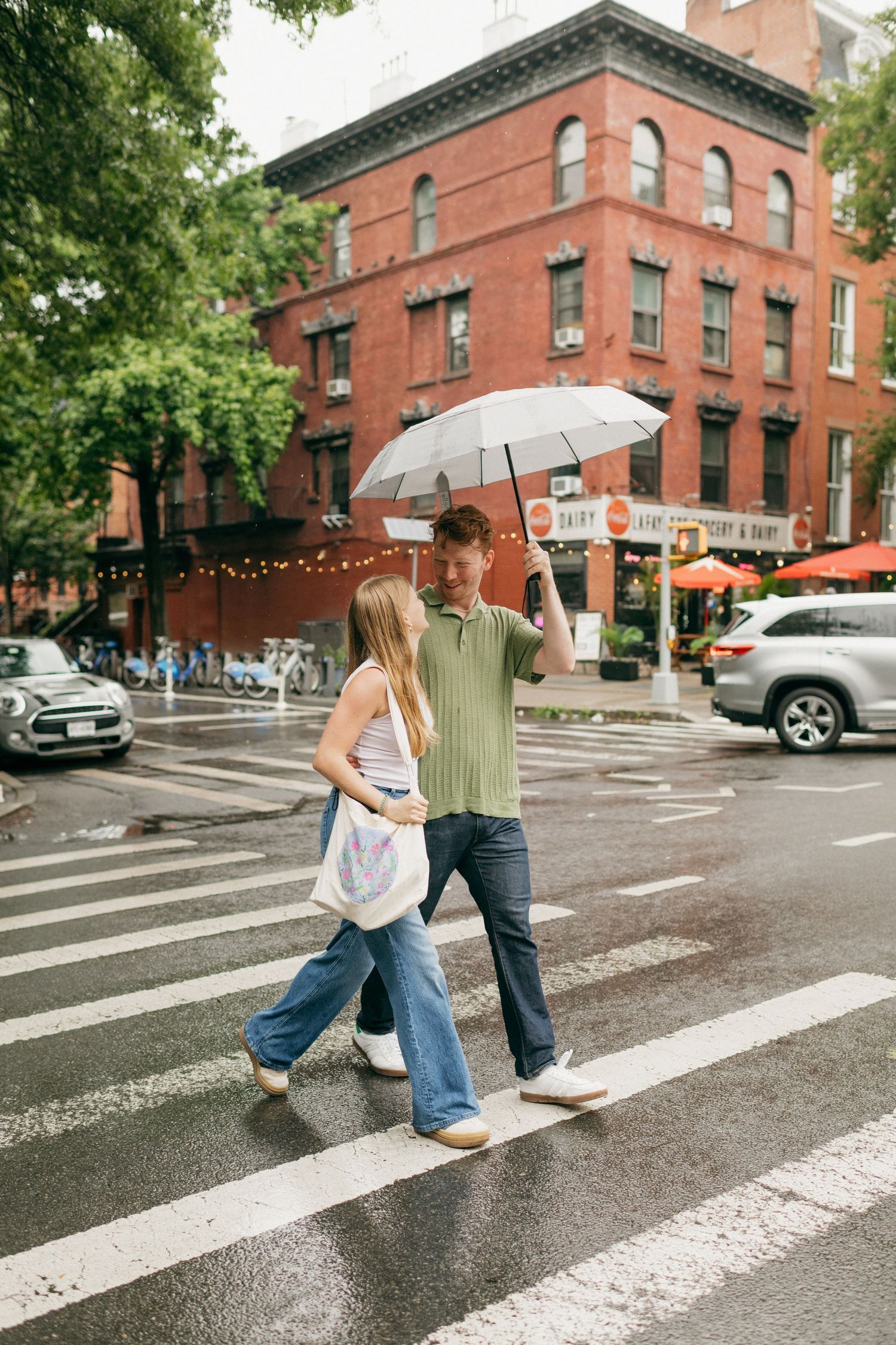 A couple crosses a rainy street in New York City while sharing an umbrella.