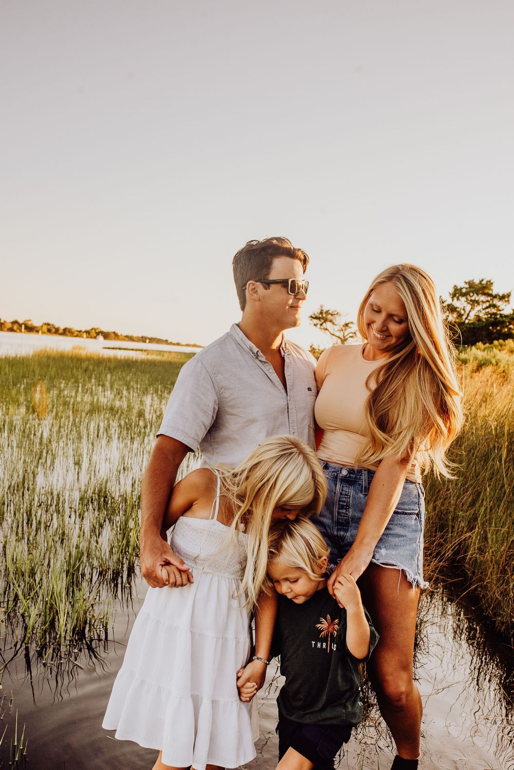 Family enjoying sunset together in marsh grass along coastal waterway during golden hour photo session.