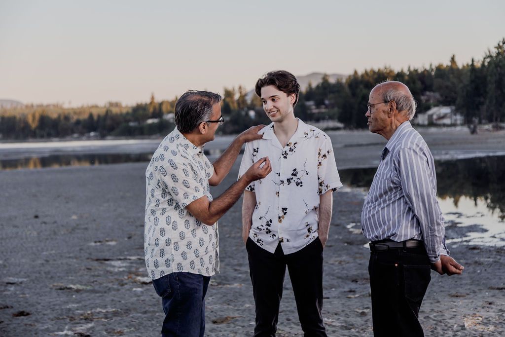 Three men laugh and interact on a rocky beach at sunset, sharing a joyful candid moment together.