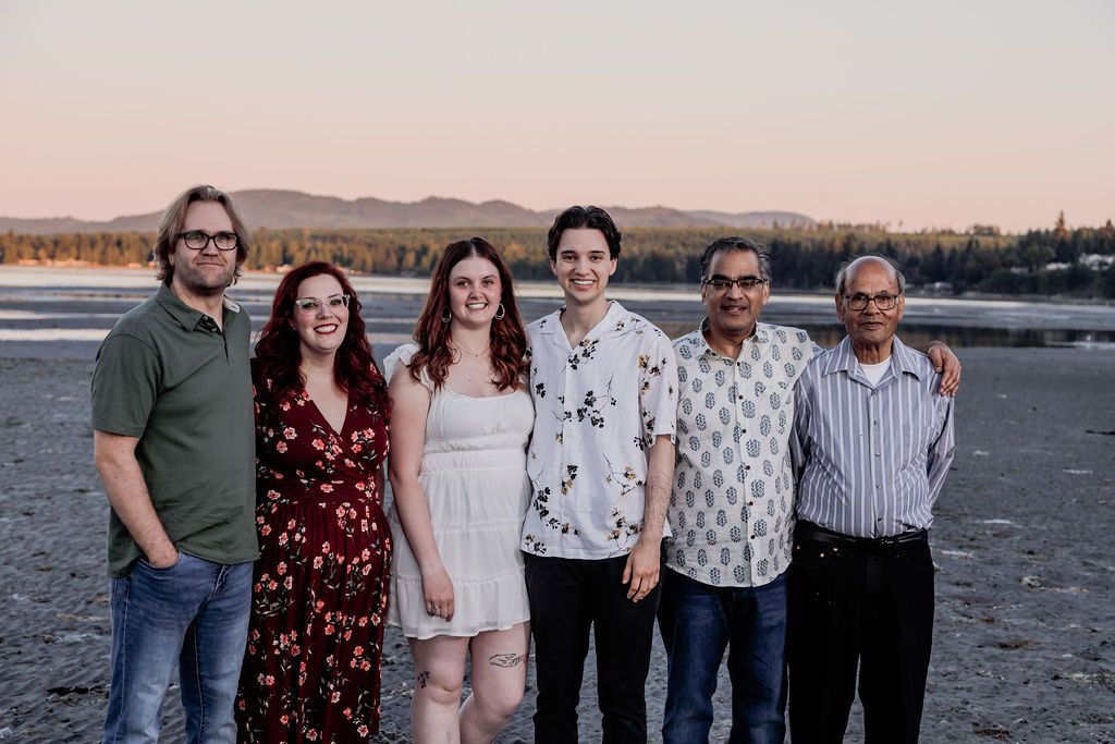 Group of six people smiling together on a beach at sunset with mountains in the background.