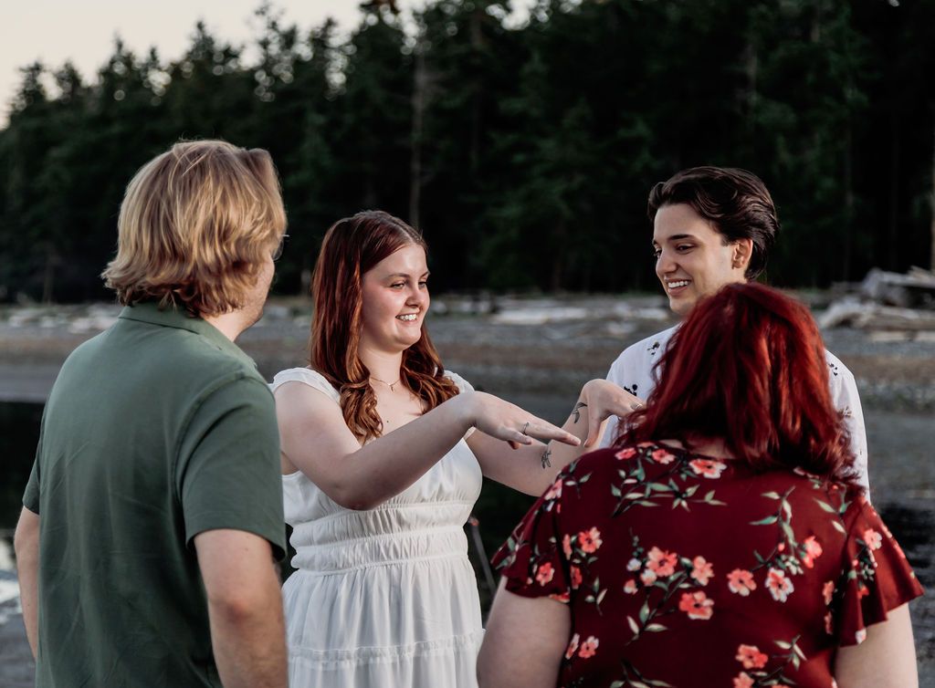 Four people gathered on a rocky beach at dusk, two women holding hands and smiling.