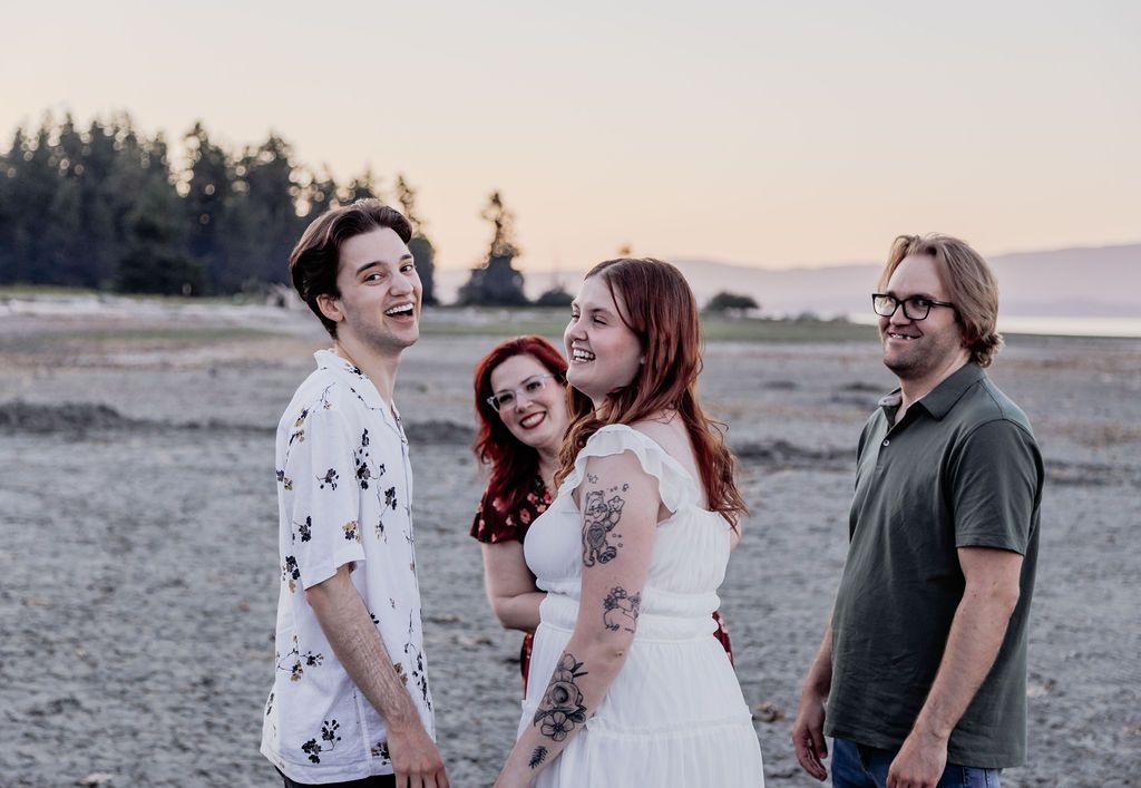 Four people laughing together on a sandy beach during golden hour sunset.