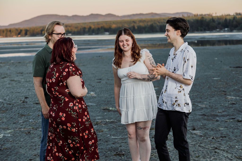 Four people having a joyful conversation on a beach at sunset with mountains behind them.