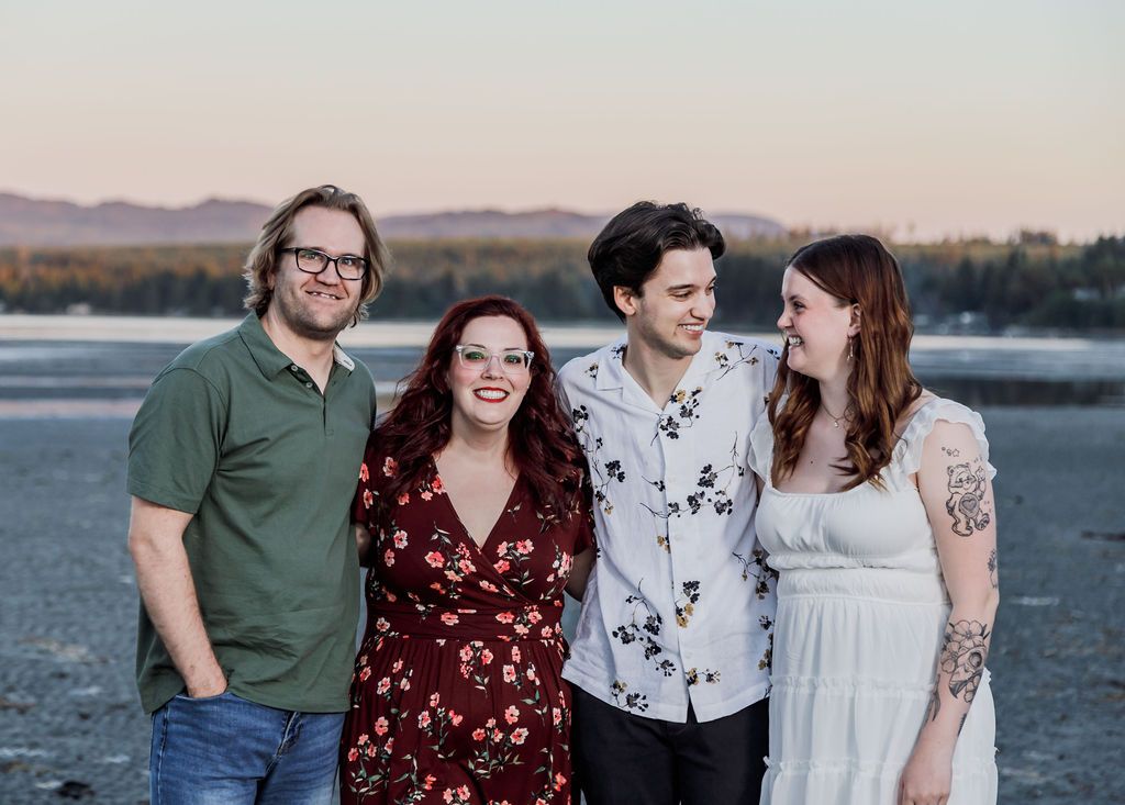 Four smiling people posing together on a beach at sunset with scenic mountain backdrop.