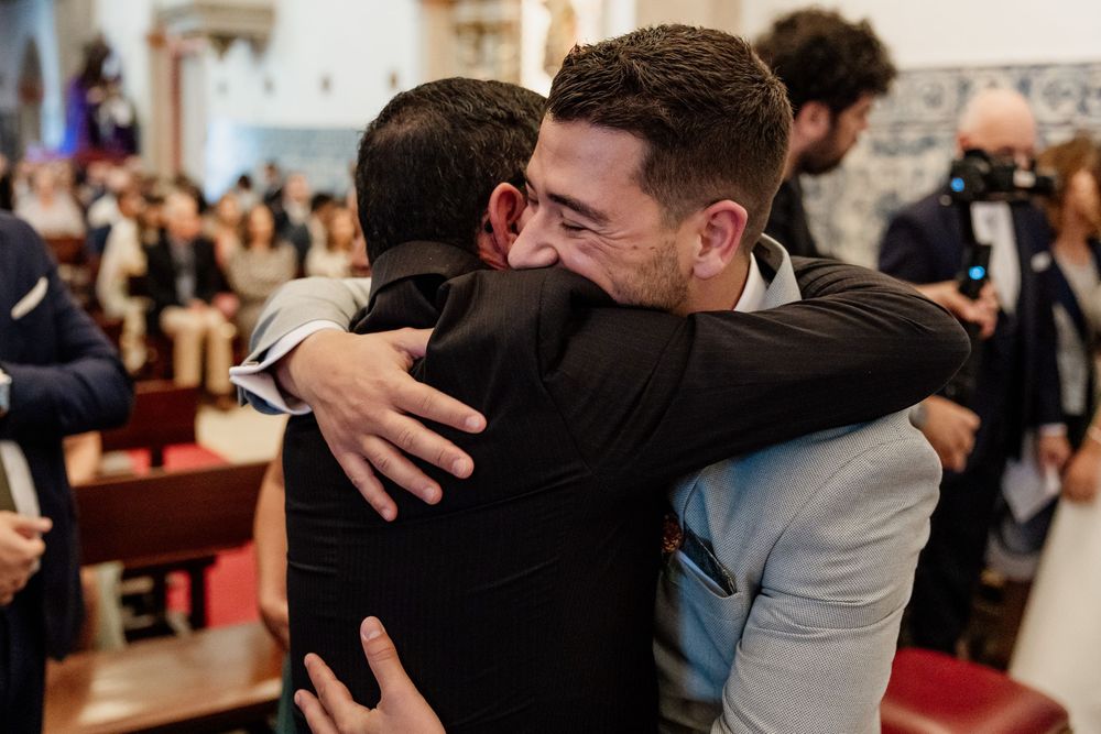 Two men share an emotional hug inside a church during a wedding ceremony.