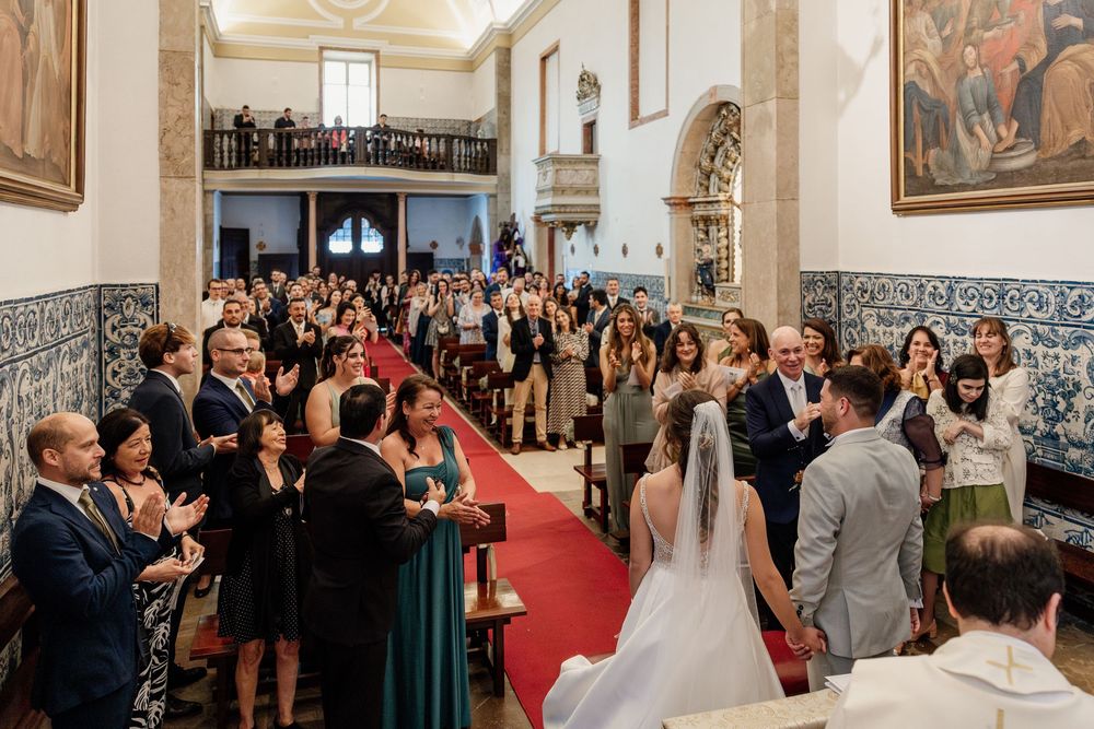 Bride and groom at church altar surrounded by applauding guests during a traditional wedding ceremony with red carpet aisle.