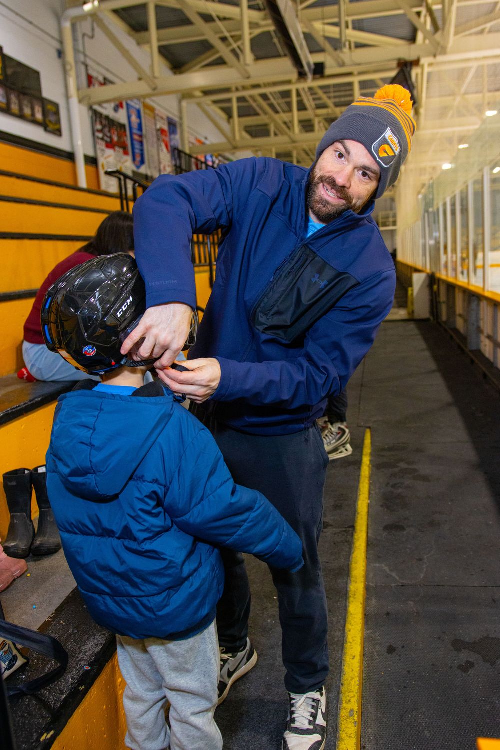 Person in blue uniform tying ice skates in a hockey rink hallway.