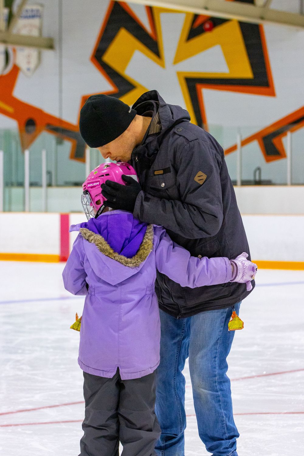 Parent and child sharing a tender moment while ice skating at an indoor rink.