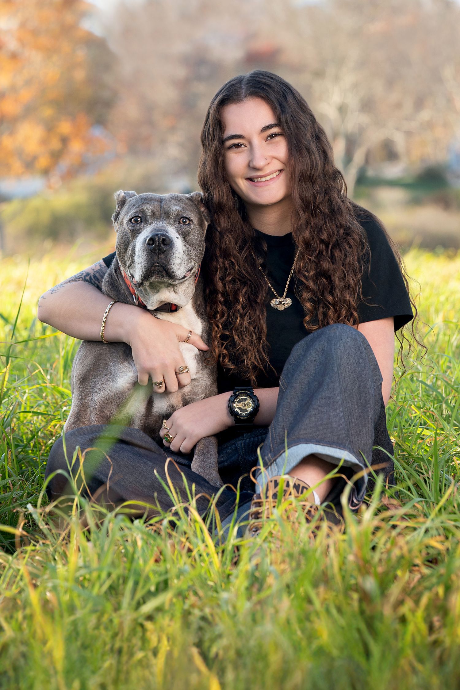 A person in a black shirt sits with their husky dog in a grassy field during autumn.
