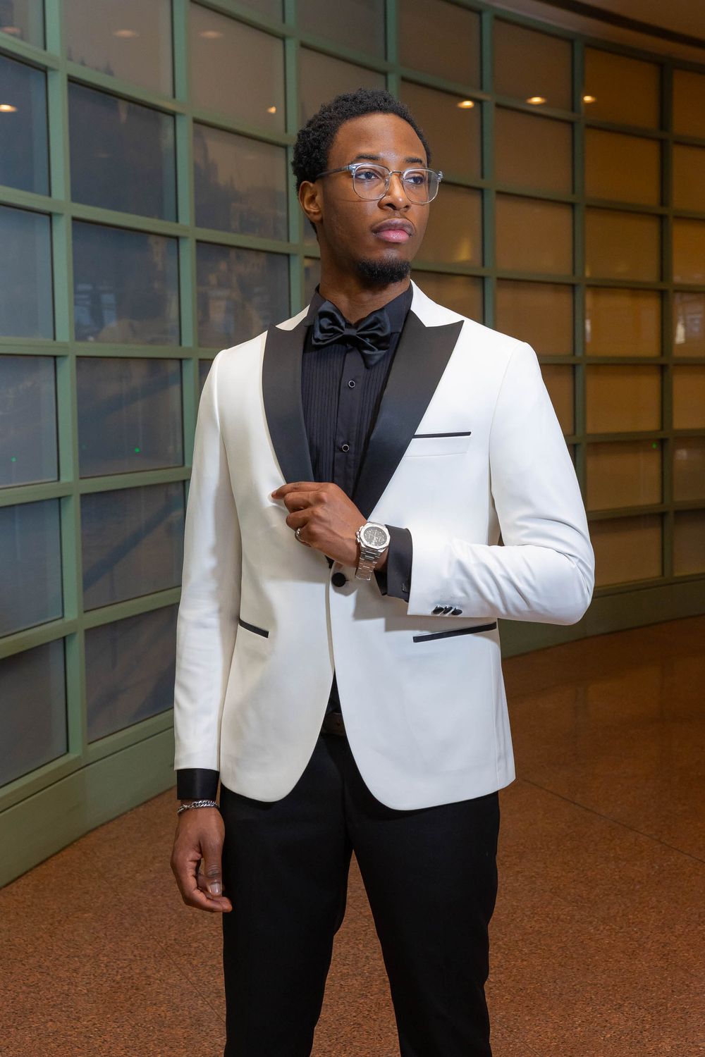A person wearing a formal white dinner jacket and black bow tie stands in an elegant indoor setting.