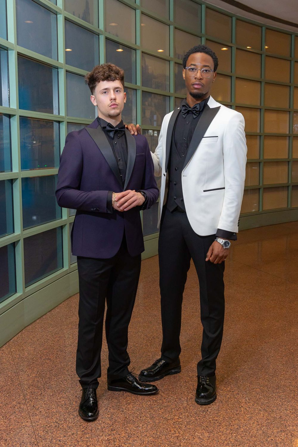 A sequence of formal dress shoes and pant legs photographed against a brown floor with green walls.