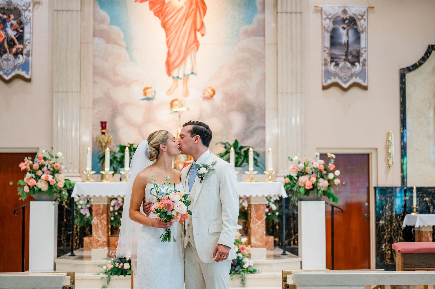 A romantic wedding couple shares a tender moment in a beautiful church sanctuary with stained glass windows and flowers.