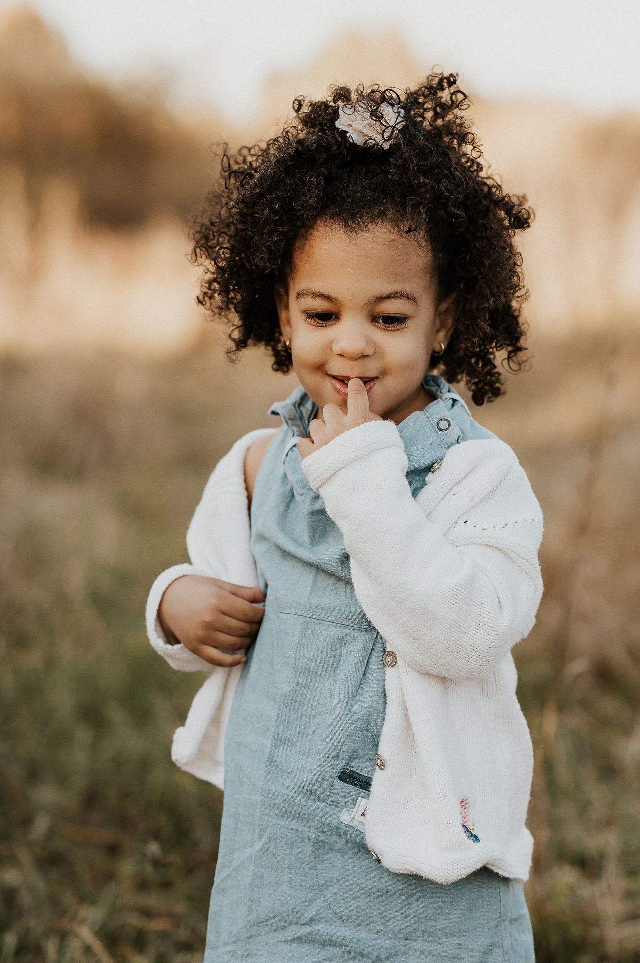 Enfant debout en extérieur dans des herbes hautes, vêtement pâle et arrière-plan flou.