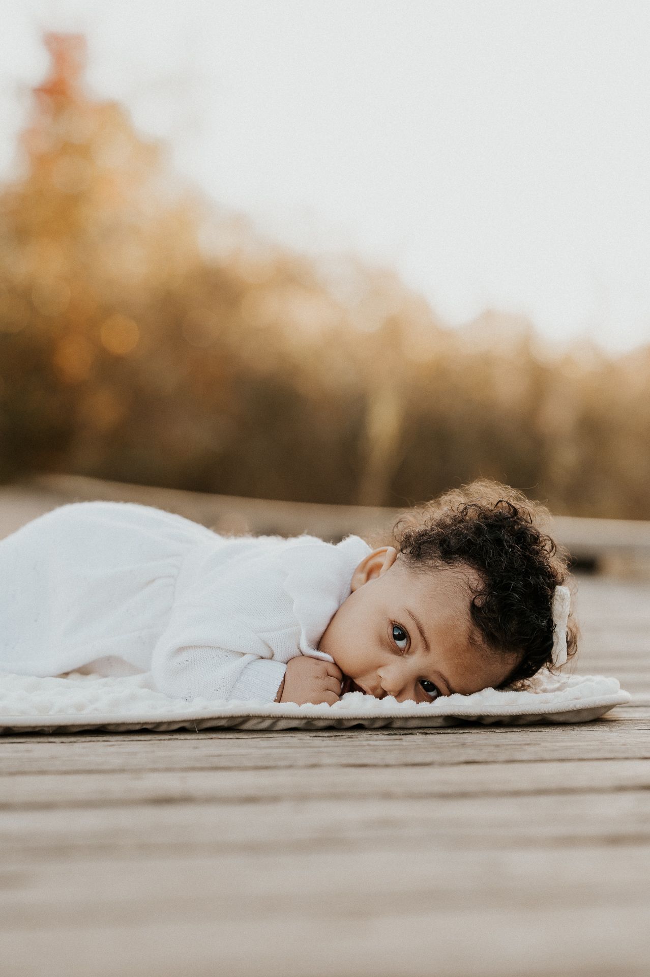 Enfant allongé sur une surface en bois en extérieur, herbes hautes en arrière-plan.