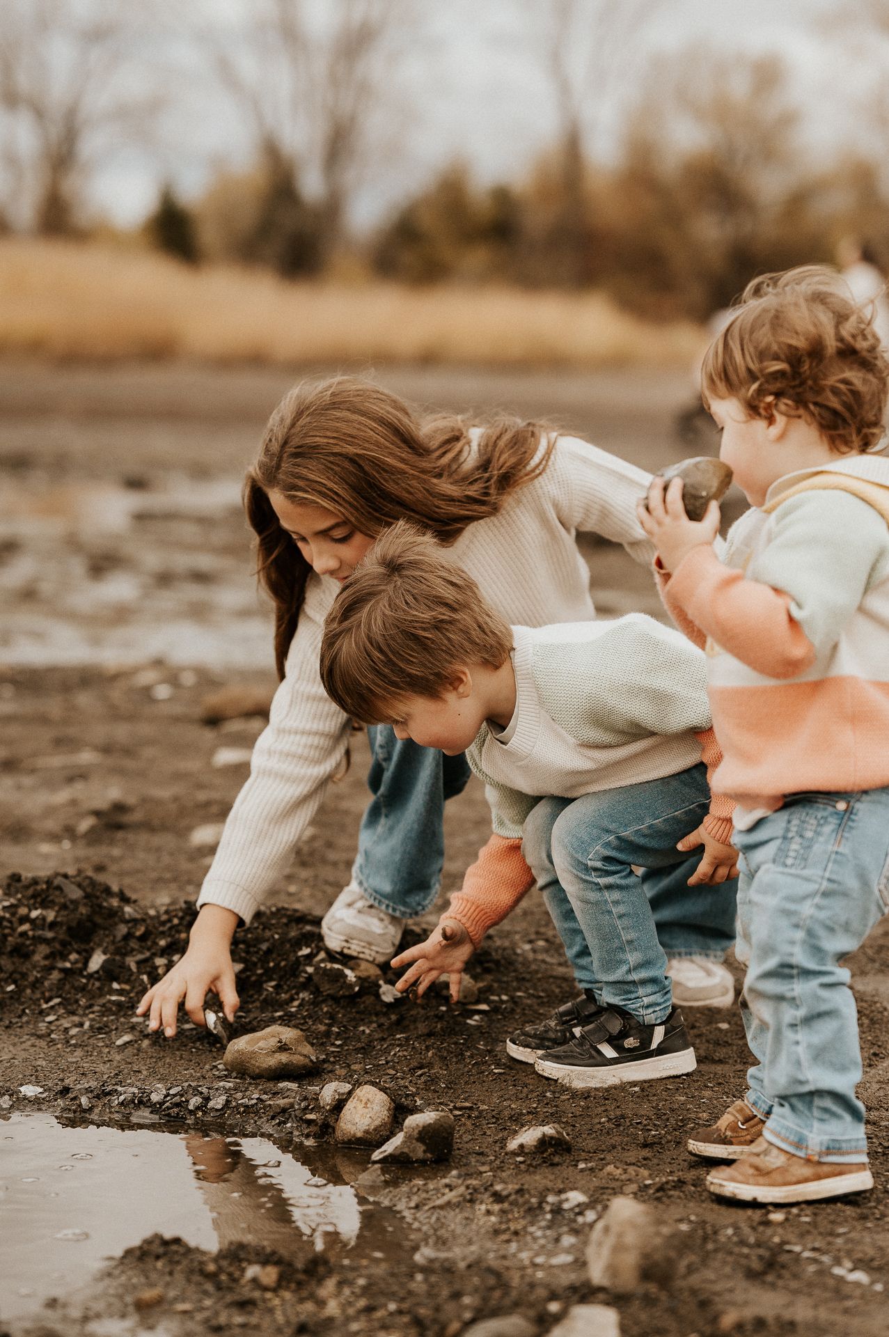 Trois enfants au bord de l’eau, jouant avec des pierres sur la rive-sud de Montréal.