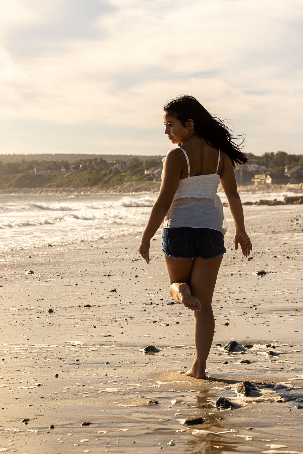 A person walks along a rocky beach shoreline on a cloudy day searching the sand and stones.