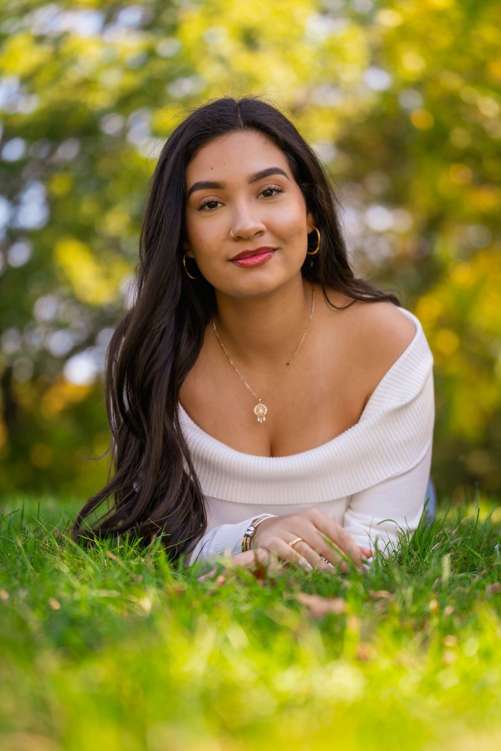 Young woman in white sweater poses on grass with soft autumn bokeh background.