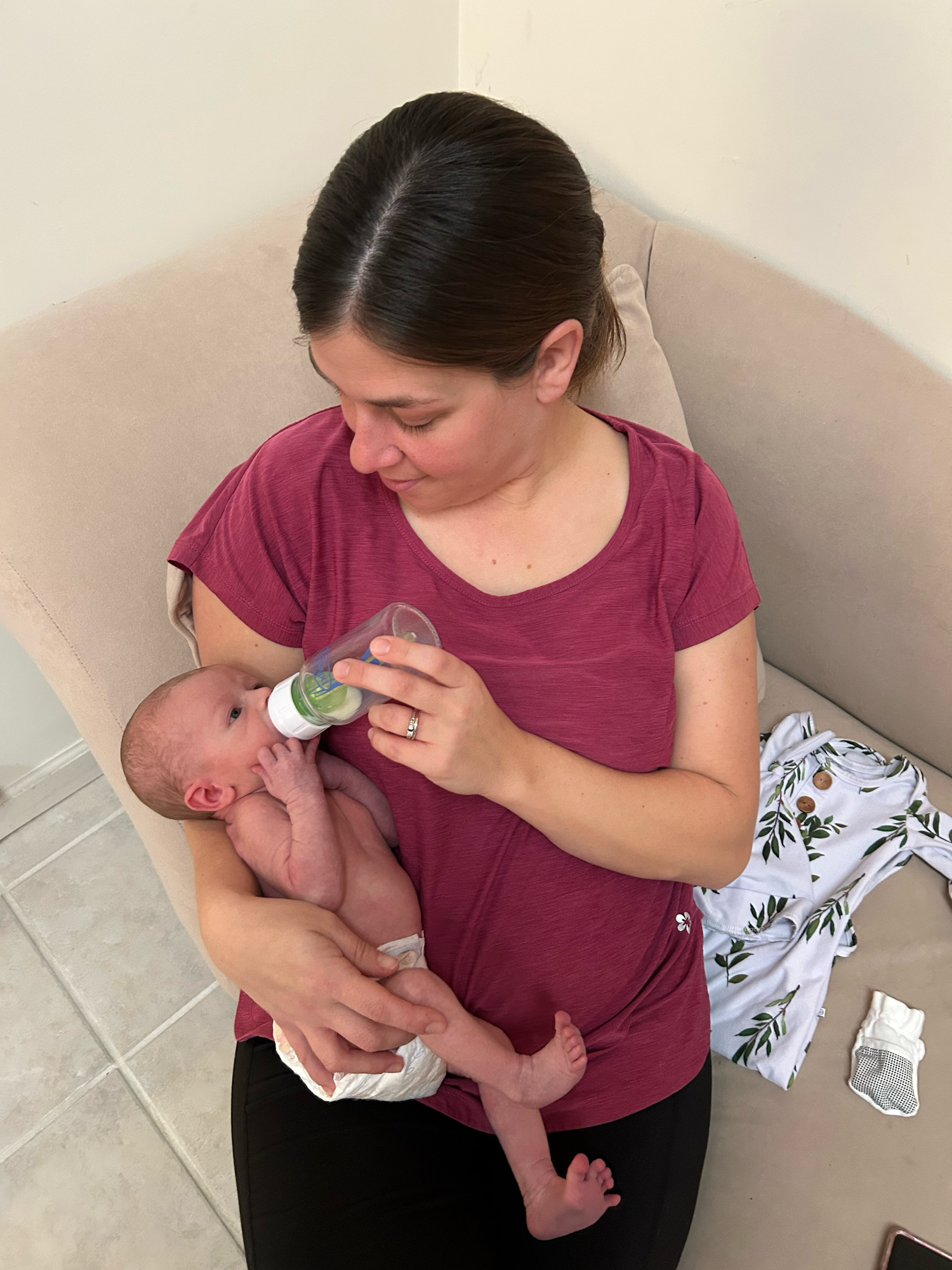 A parent in a burgundy shirt bottle feeds an infant while sitting on a tiled floor in a series of photos.