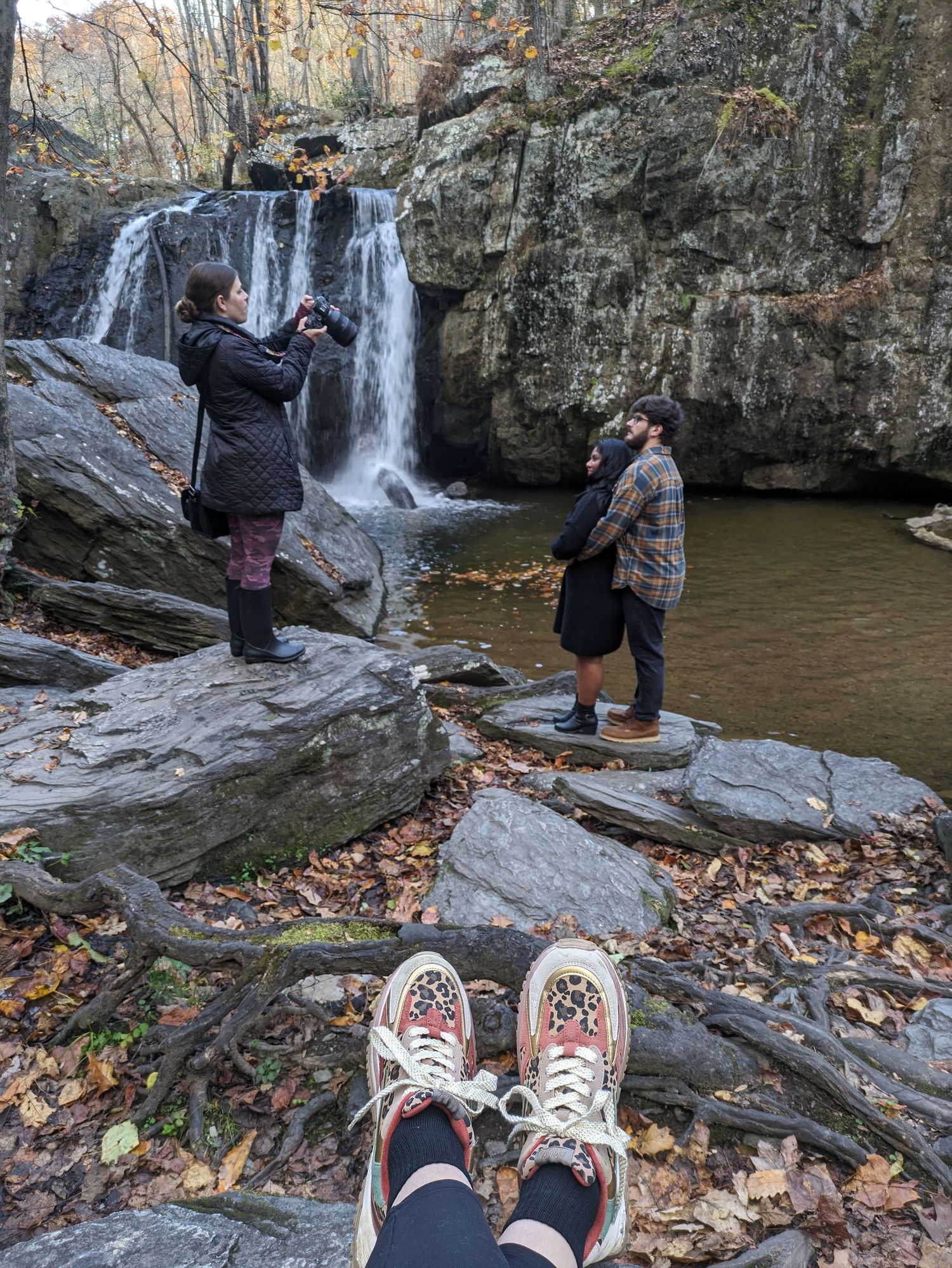 Hikers explore a scenic waterfall surrounded by autumn foliage and rocky cliffs at a state park.