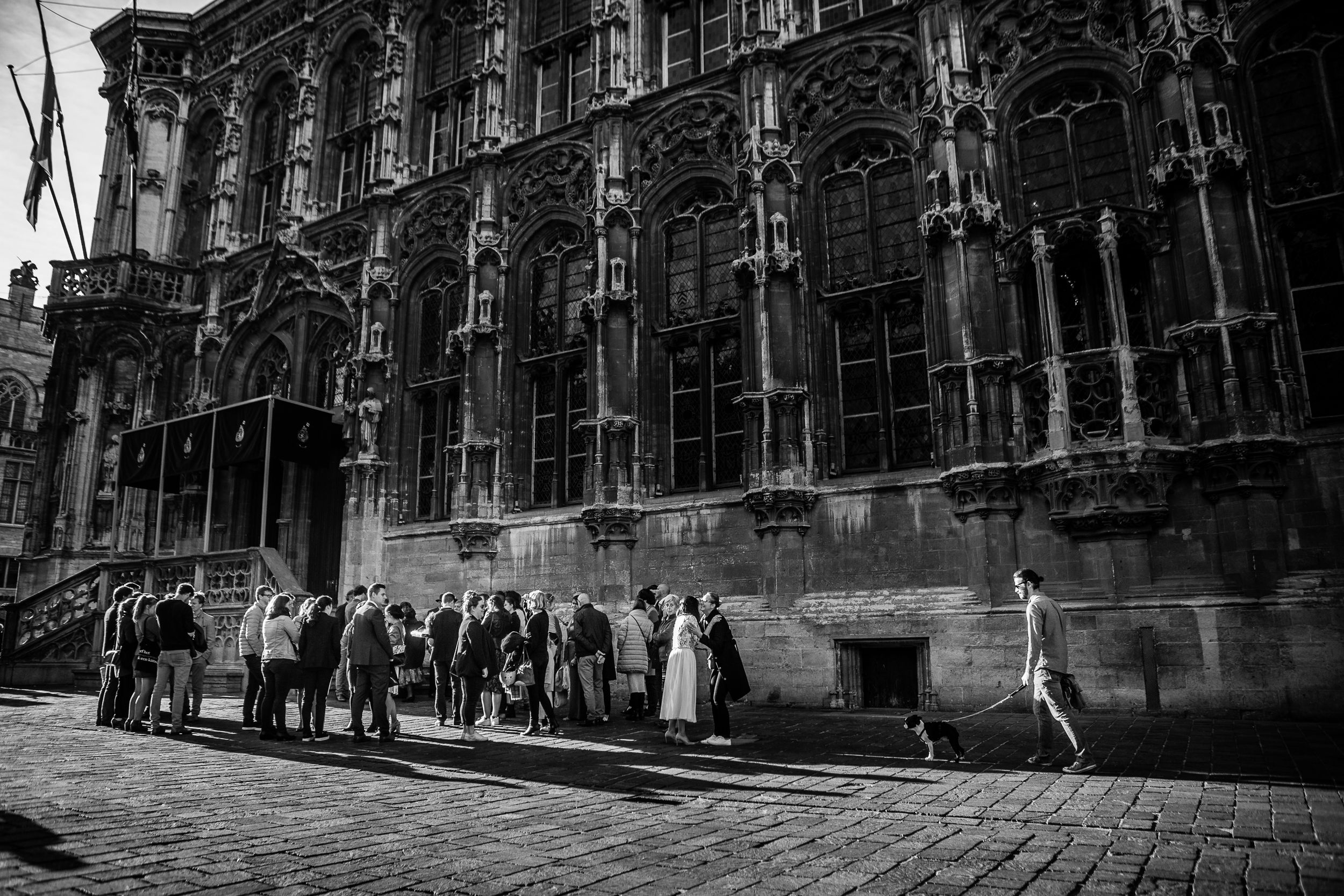 Guests gather in a sunlit cobblestone courtyard during an outdoor wedding ceremony in a historic European building.