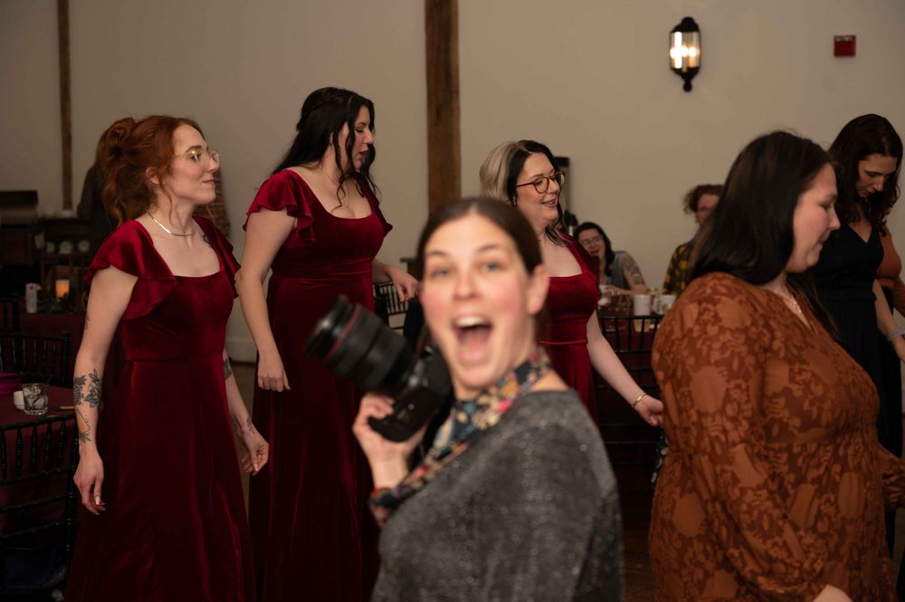 A group of people in burgundy velvet dresses and formal attire dancing and celebrating at an indoor event.