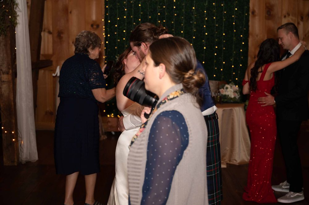 Wedding guests dance and celebrate during an evening reception with twinkle lights and white drapes in the background.