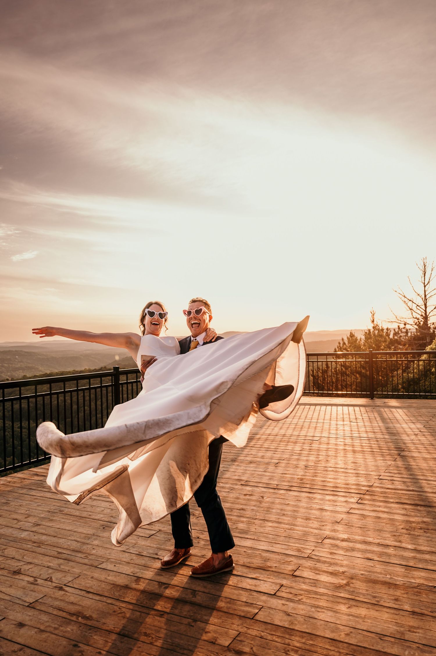 A couple performs a romantic dip dance pose on a wooden deck at sunset with warm golden lighting.