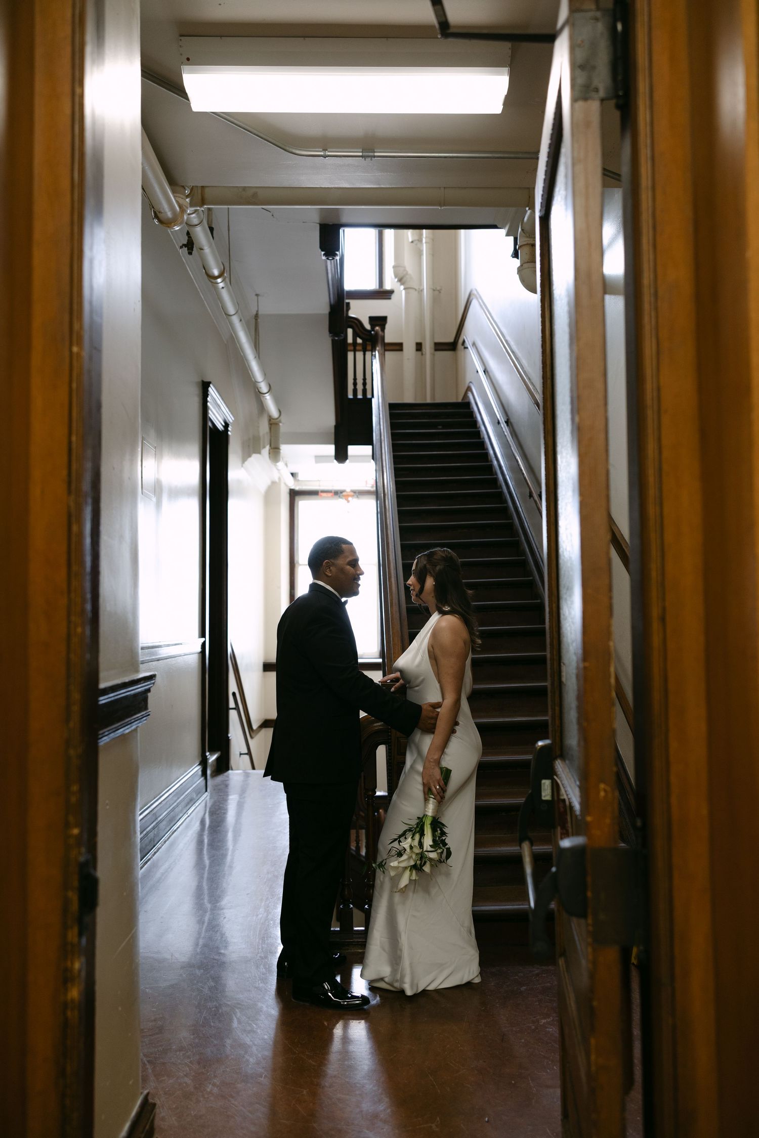 A sequence of four wedding photos showing a couple walking through a hallway with wooden columns and stairs.