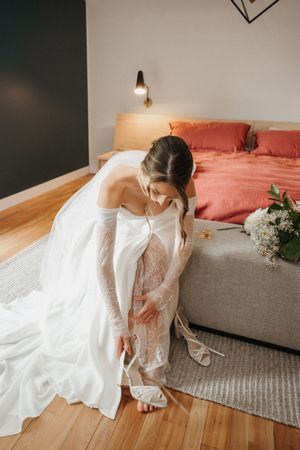 A flowing white wedding dress swirls gracefully across hardwood floors in a bedroom with coral accents and natural light.