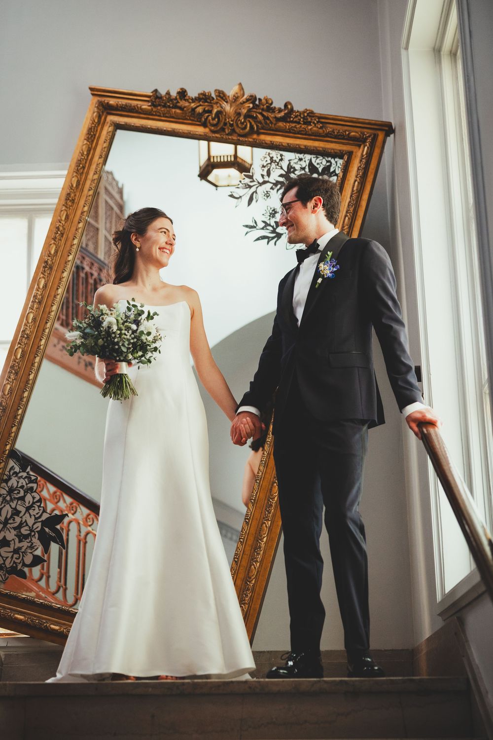 A bride and groom pose together in a bright room with an ornate gold mirror creating artistic wedding portraits at the Line DC