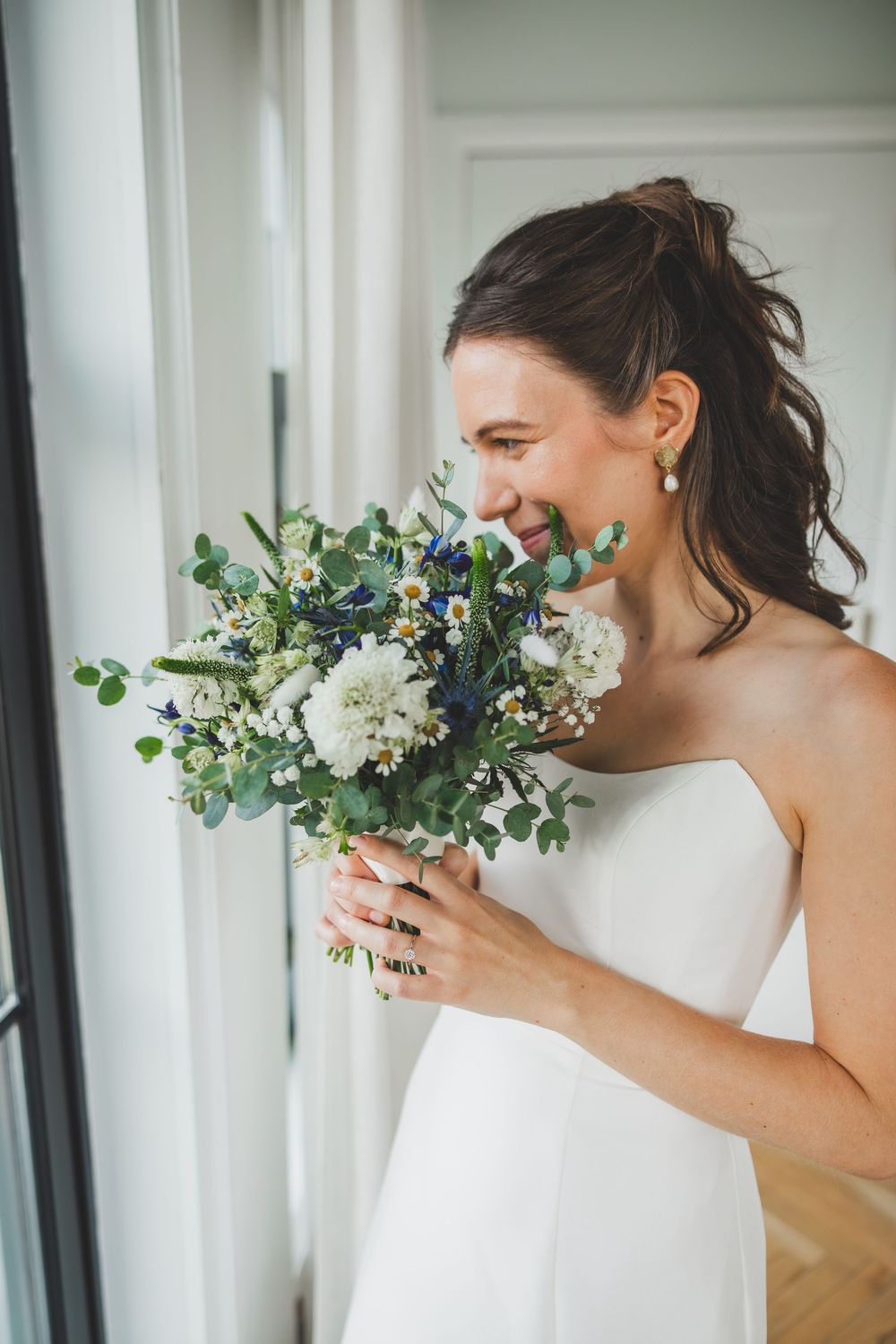 A bride in an elegant white dress smiles while holding a romantic bouquet of white flowers and eucalyptus before her the line dc wedding