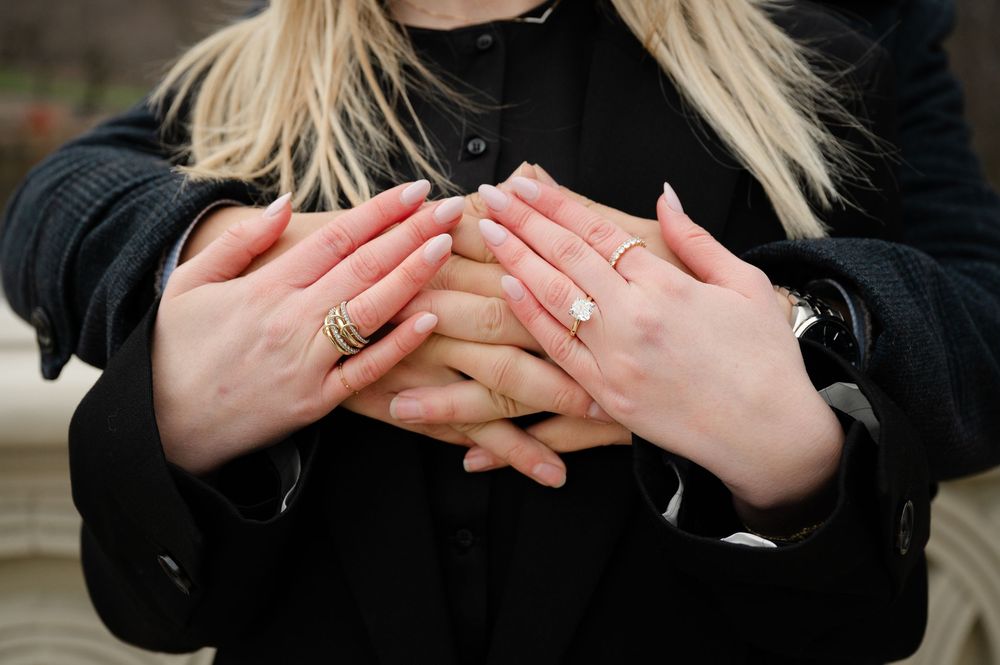 Hands with white manicured nails crossed over chest wearing a black sweater in natural lighting.
