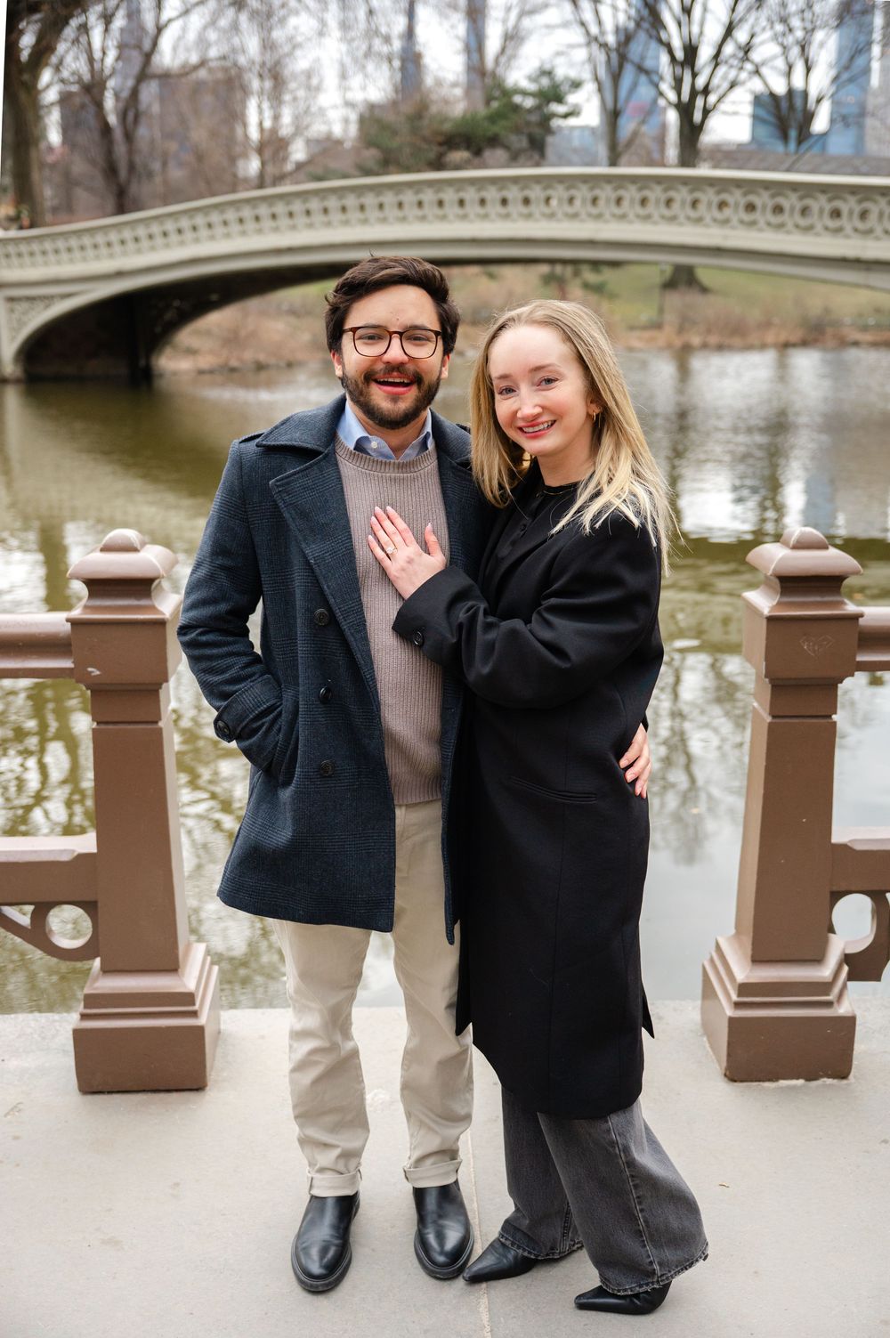 A couple celebrates their engagement on a bridge overlooking a lake in Central Park.