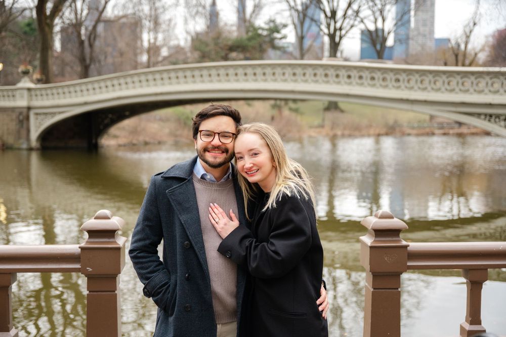 A couple embraces while standing by the iconic Bow Bridge in Central Park on a winter afternoon.