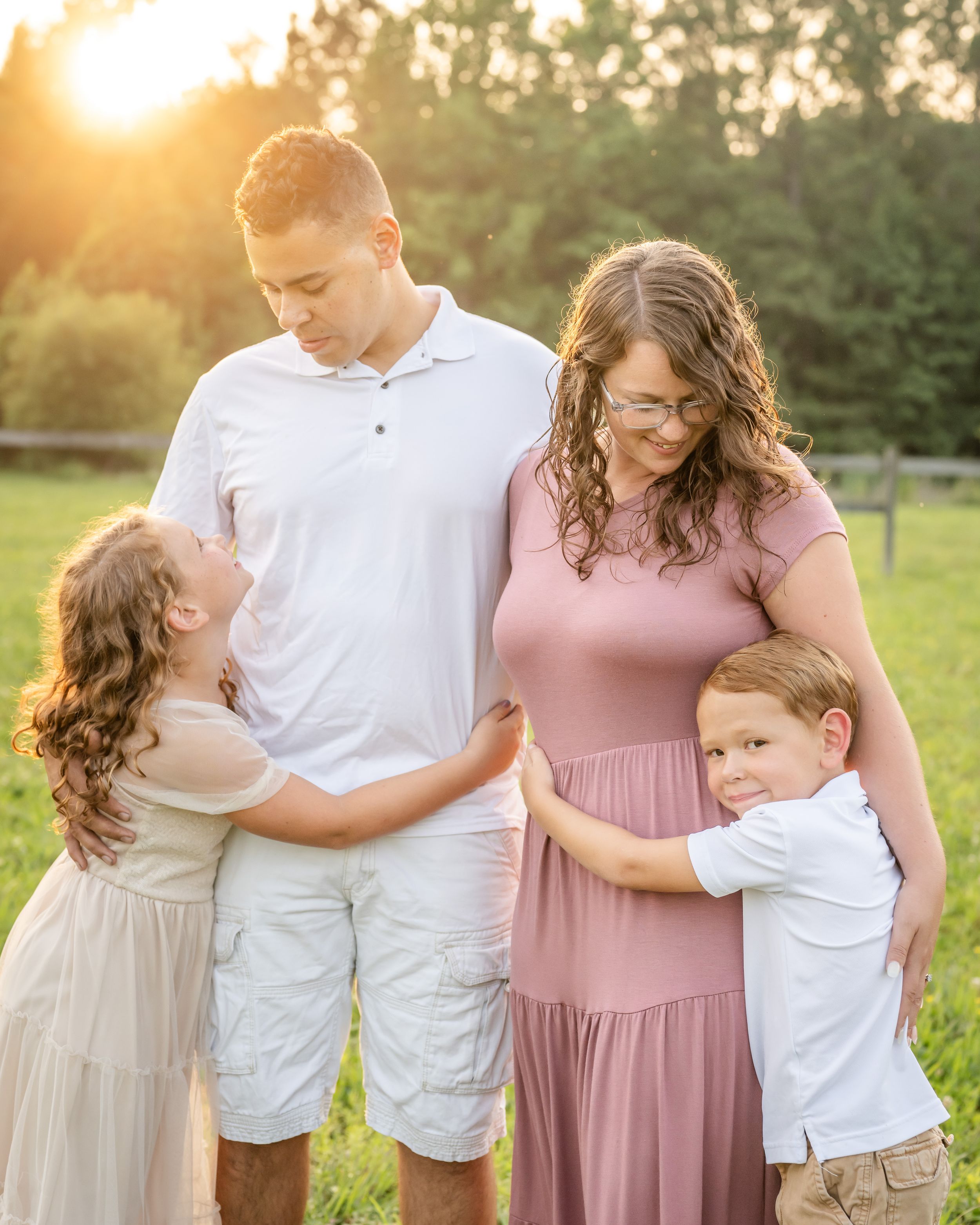 A family in coordinated pink and white outfits poses together in a sunlit field during golden hour.