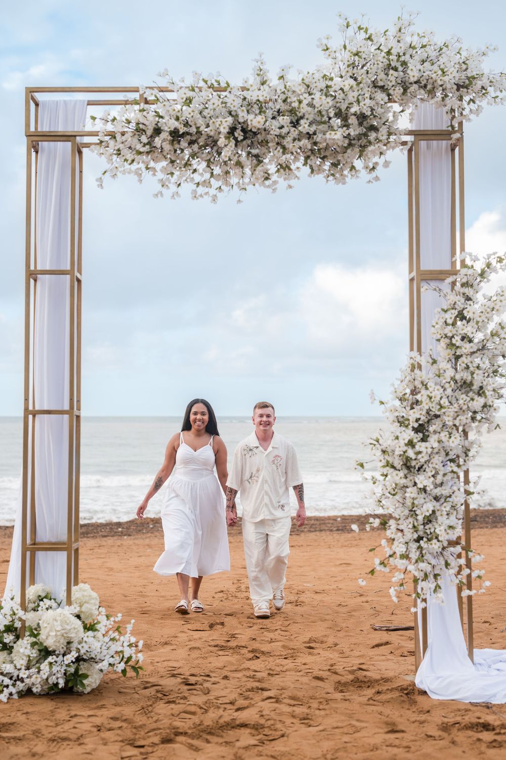 Couple walking along beach near floral arch during engagement session at Wyndham Grand Rio Mar