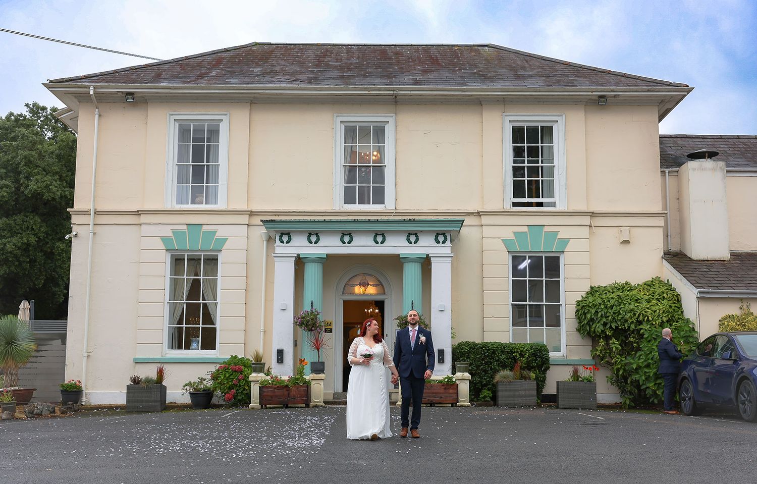 Bride and groom posing together outside an elegant cream-colored manor house venue on their wedding day.