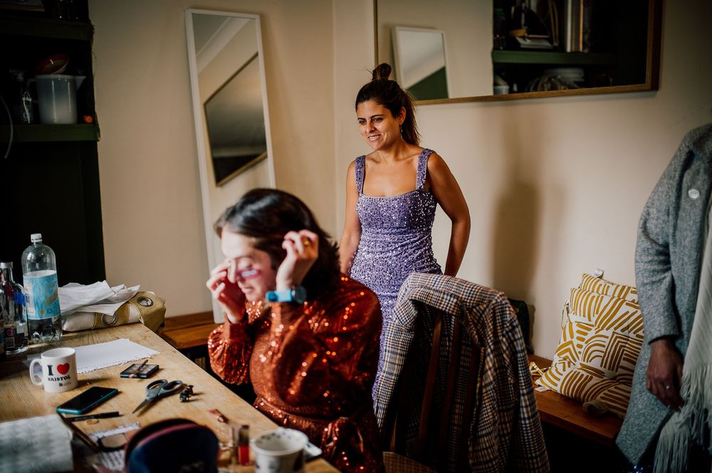 Woman in checkered dress sits at desk with laptop while working from home in bright sunlit room.