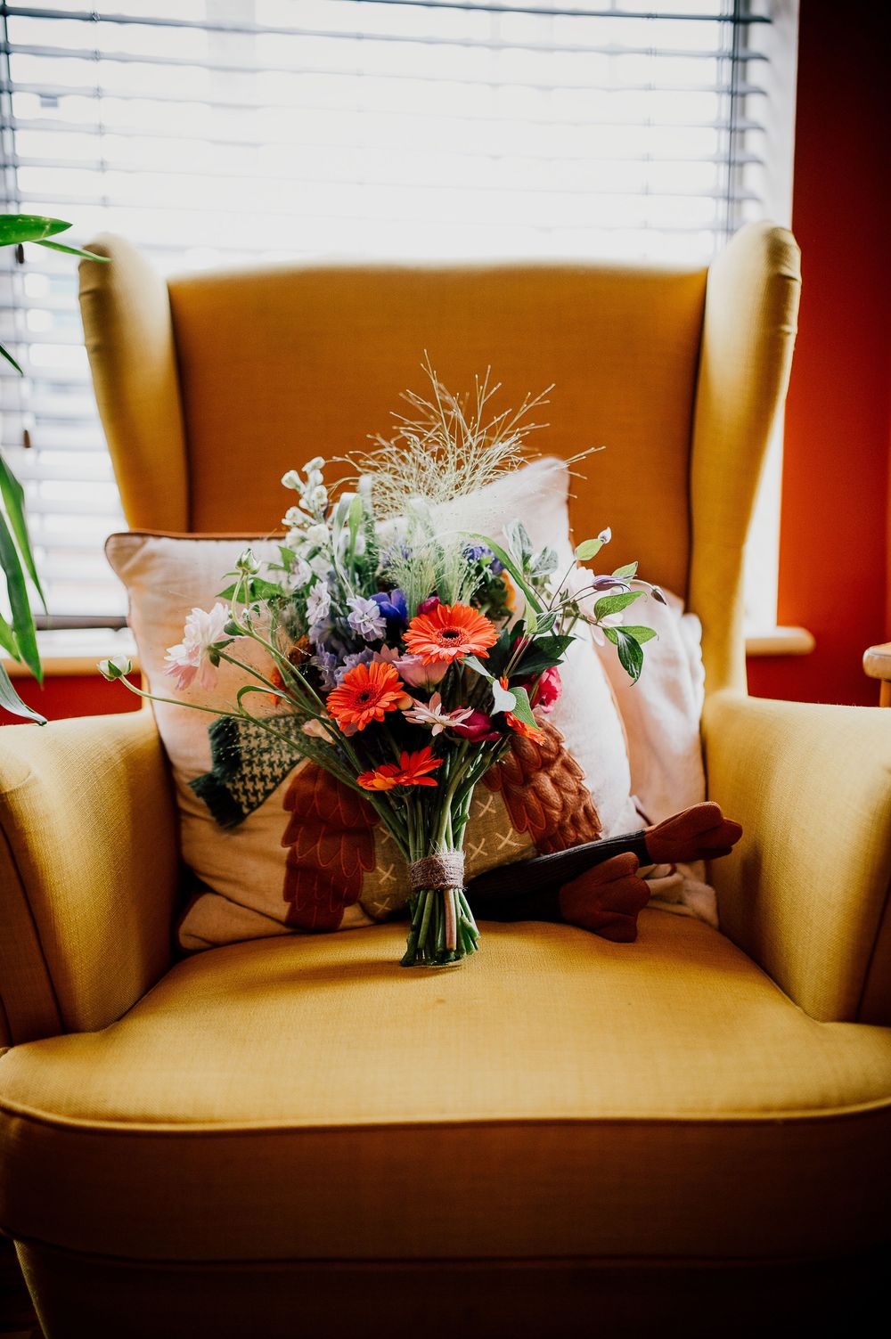 Colorful floral bouquets arranged on a beige couch against window blinds create an elegant display.