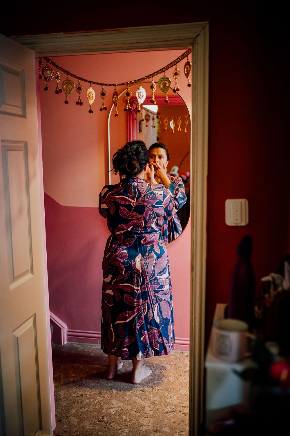 A person in a blue floral robe stands in a doorway with festive decorations hanging above in a pink-walled room.