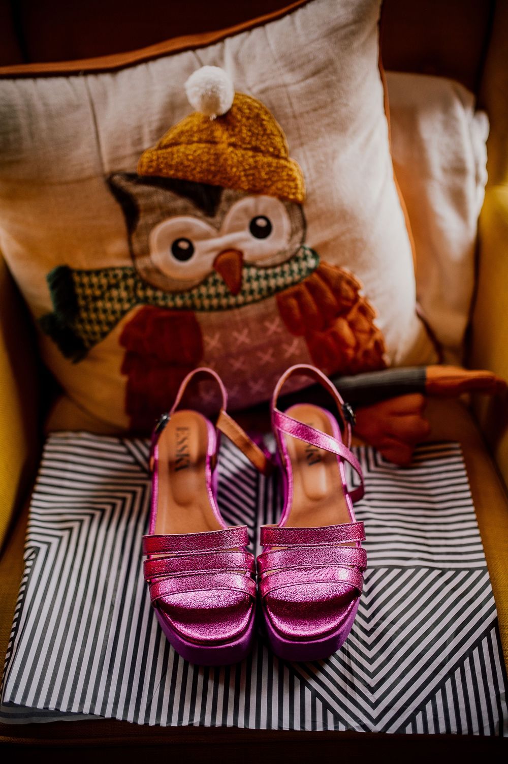 Pink metallic sandals displayed on black and white striped fabric with a plush toy in the background.